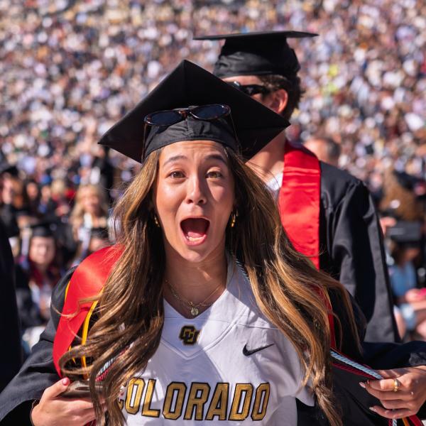 Student showing off Buffs football jersey underneath cap and gown