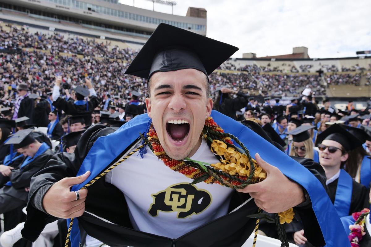 A CU student opening their gown to show a CU T-shirt underneath