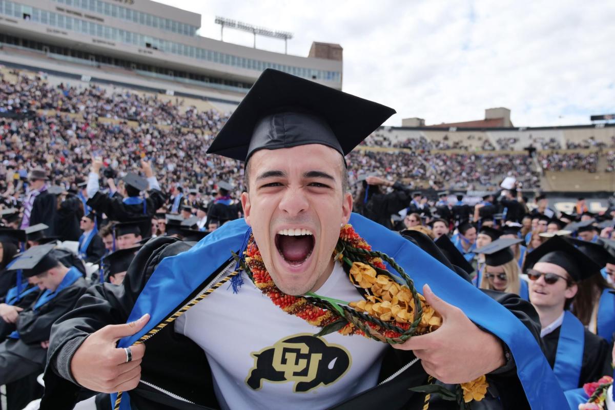 Student pulling back his gown to show a CU shirt underneath