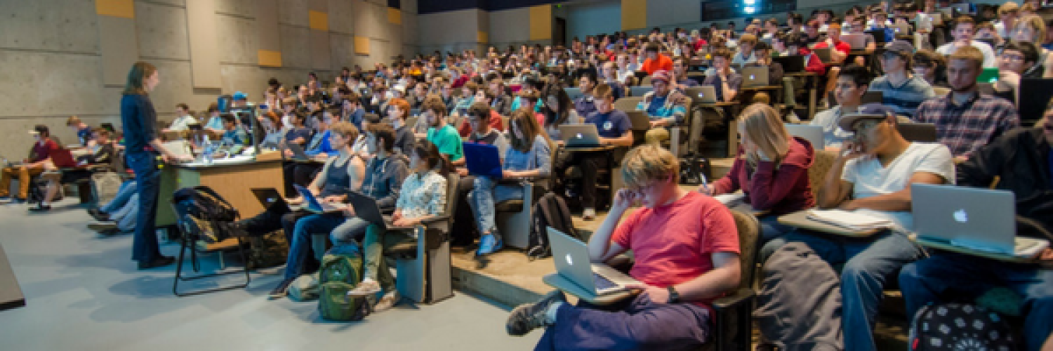 Students listening to professor speak in stadium-style seating lecture hall
