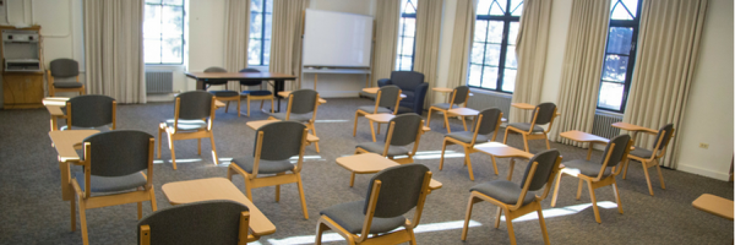 Residence hall classroom with a lot of windows, chairs with desks attached, carpet