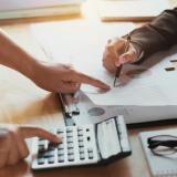 Two people leaning over a desk and looking at a calculator and paper