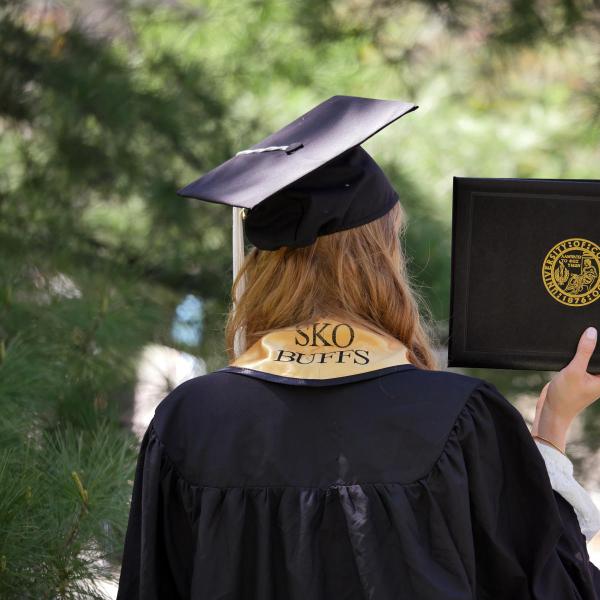 A CU grad in their cap and gown holding up their diploma