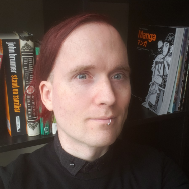 person with black shirt, red hair, and blue eyes, posing in front of a book case