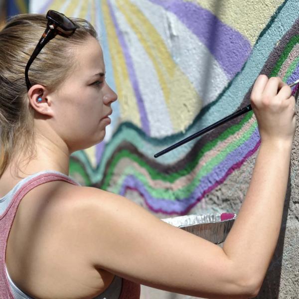 female student painting on a pastel wavy mural
