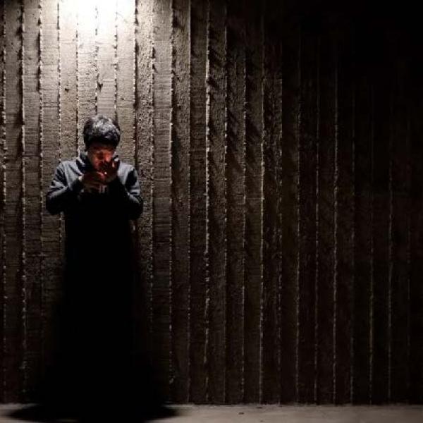 image of a person standing in front of a concrete wall under a light lighting a cigarette