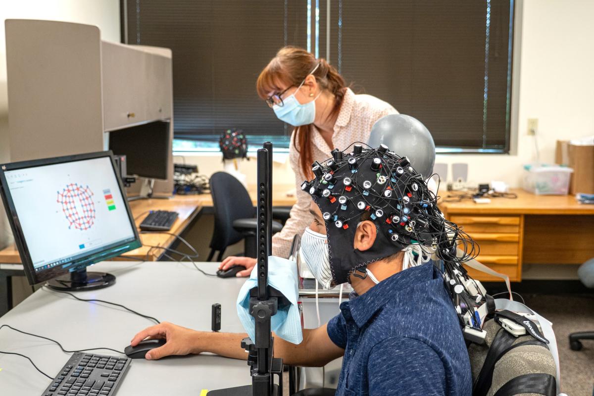 Rosy Southwell and Cooper Steputis demonstrate the use of a functional near-infrared spectroscopy device in D'Mello's lab