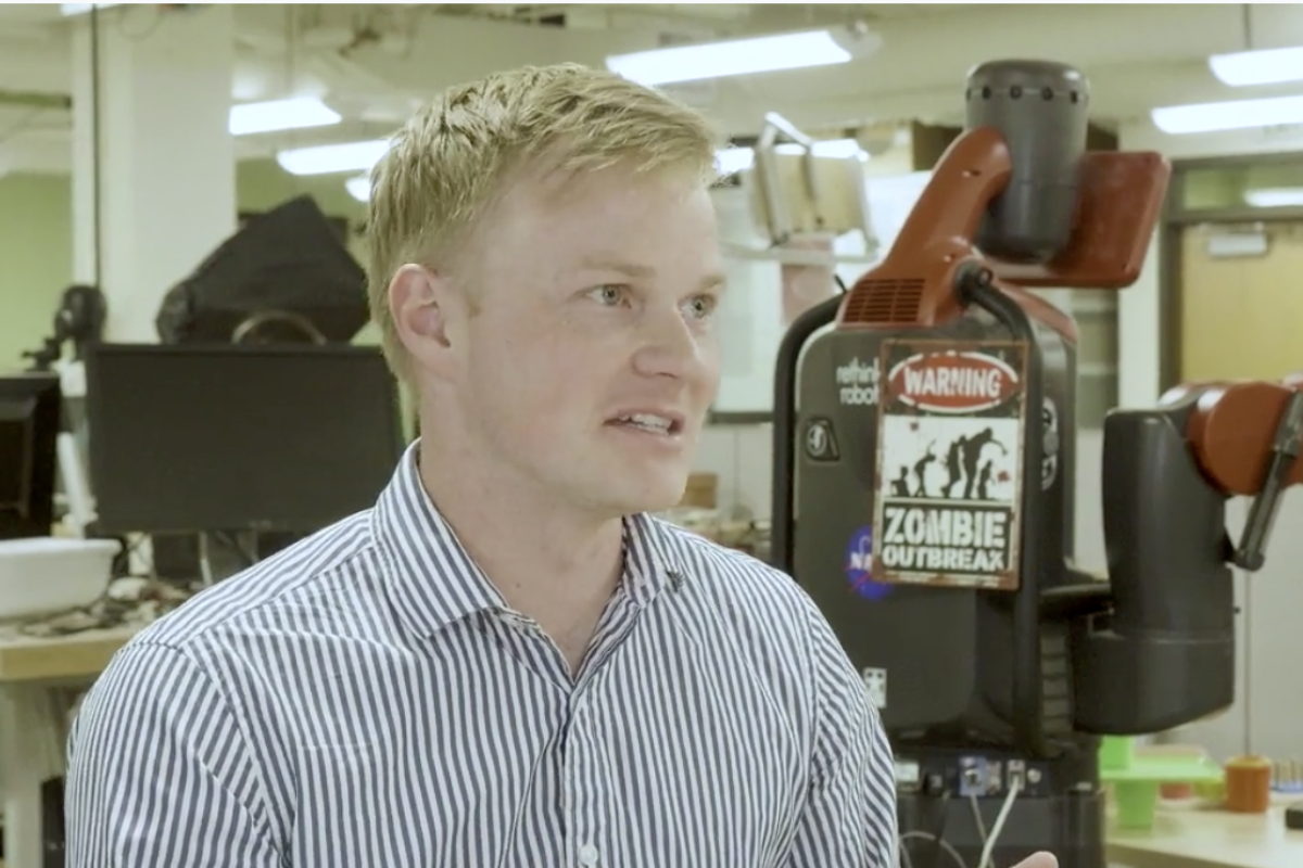 Dr. Chris Heckman, a blonde man, sits in front of a robotic arm