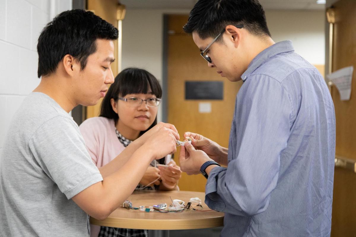 Two students show their advisor the progress they've made on a device in their lab.