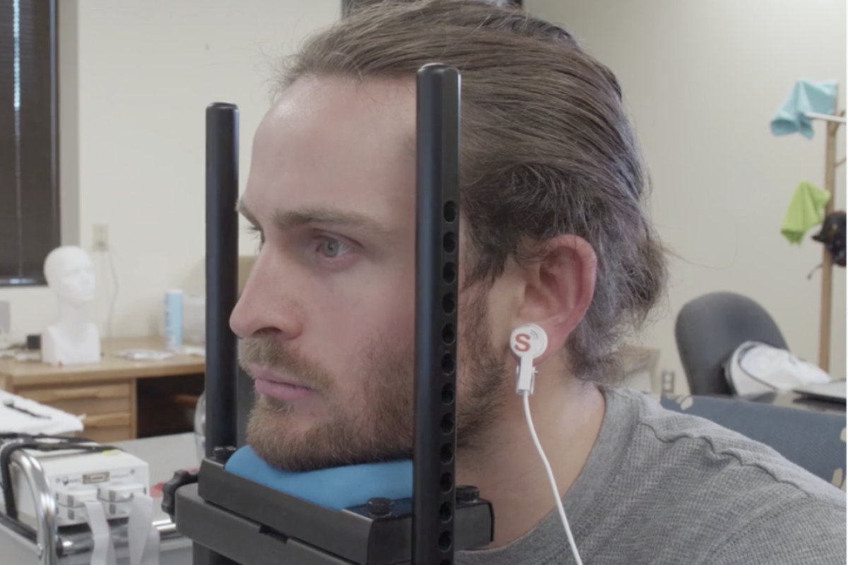 Person with long brown hair is held in a device with diodes attached to temples