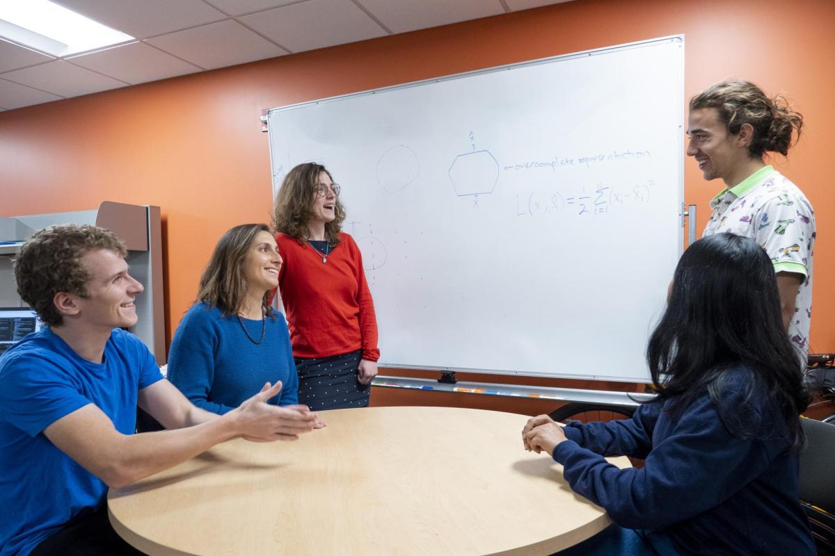 Students and their advisor discuss a problem at a whiteboard.
