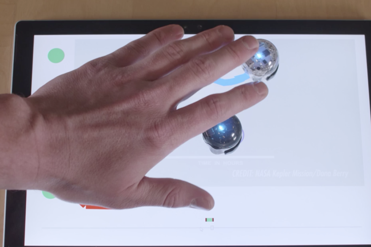 A white hand touches silver orbs attached to a screen