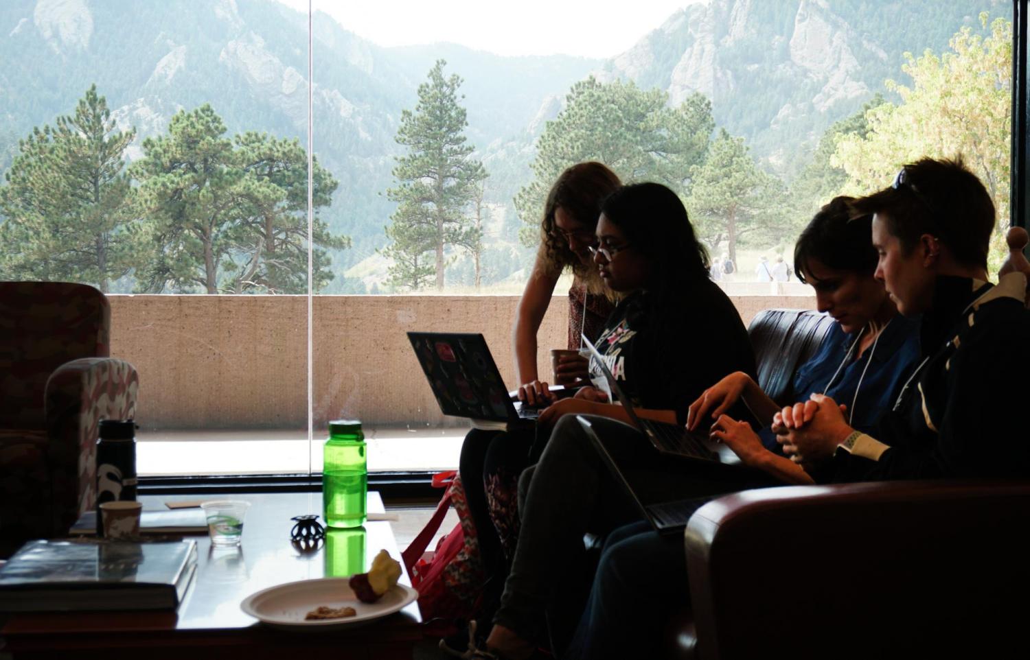 Four hackathon participants discuss their work, with Boulder's Flatirons in the background.