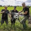 Three operators work on a drone in the middle of a grassy field.
