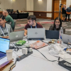 Nanog 86 hackathon participants sit at a table with computers, talking to one another