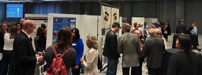 People surrounding free standing STEM Education posters in large ballroom
