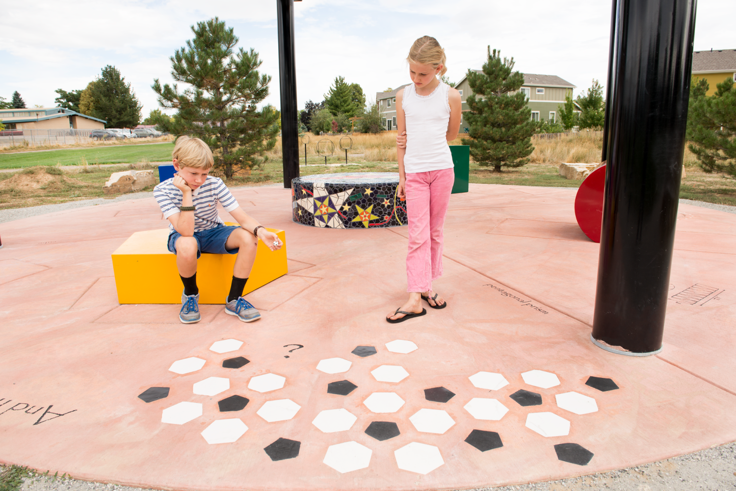 A boy and girl look at the hexagons and pentagons in the concrete