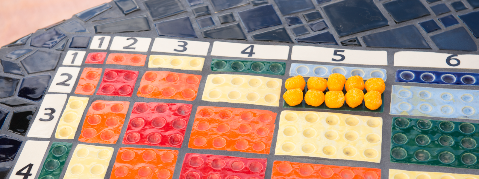 Ten cheese puffs in 2 rows of five on a mosaic multiplication table