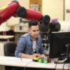Student sits at a computer underneath a robotic arm