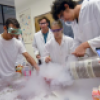 students in chemistry course working with beakers and fluids and lab coats
