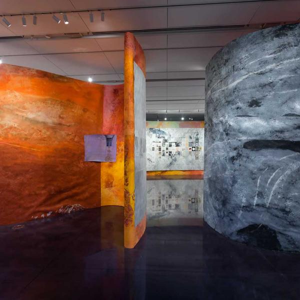 Curved walls built within the gallery, one side is bright oranges and reds, the other is shades of grey.