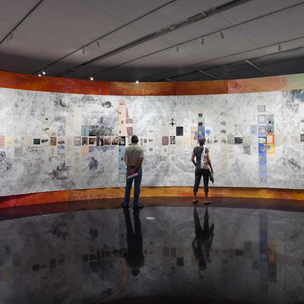 Two people stand in front of a curved wall built within the gallery.