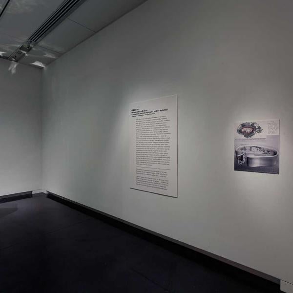 View of a mirrored object on a cylindrical pedestal with a text panel on the wall.