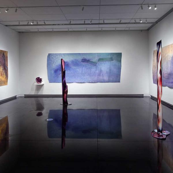 3 large paintings with tall cylindrical sculptures in the foreground.