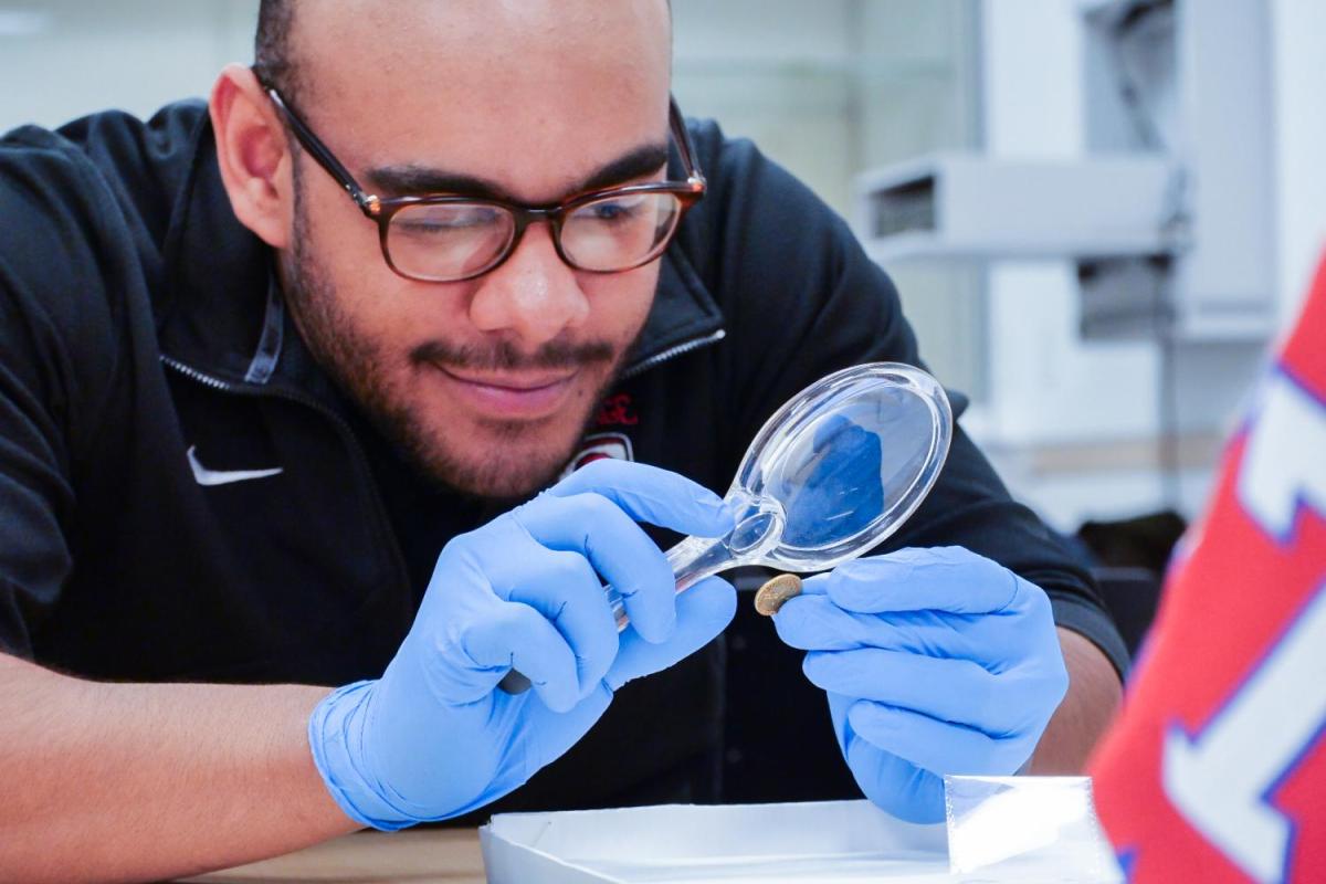 A male student uses a magnifying glass to look at the details of a gold coin