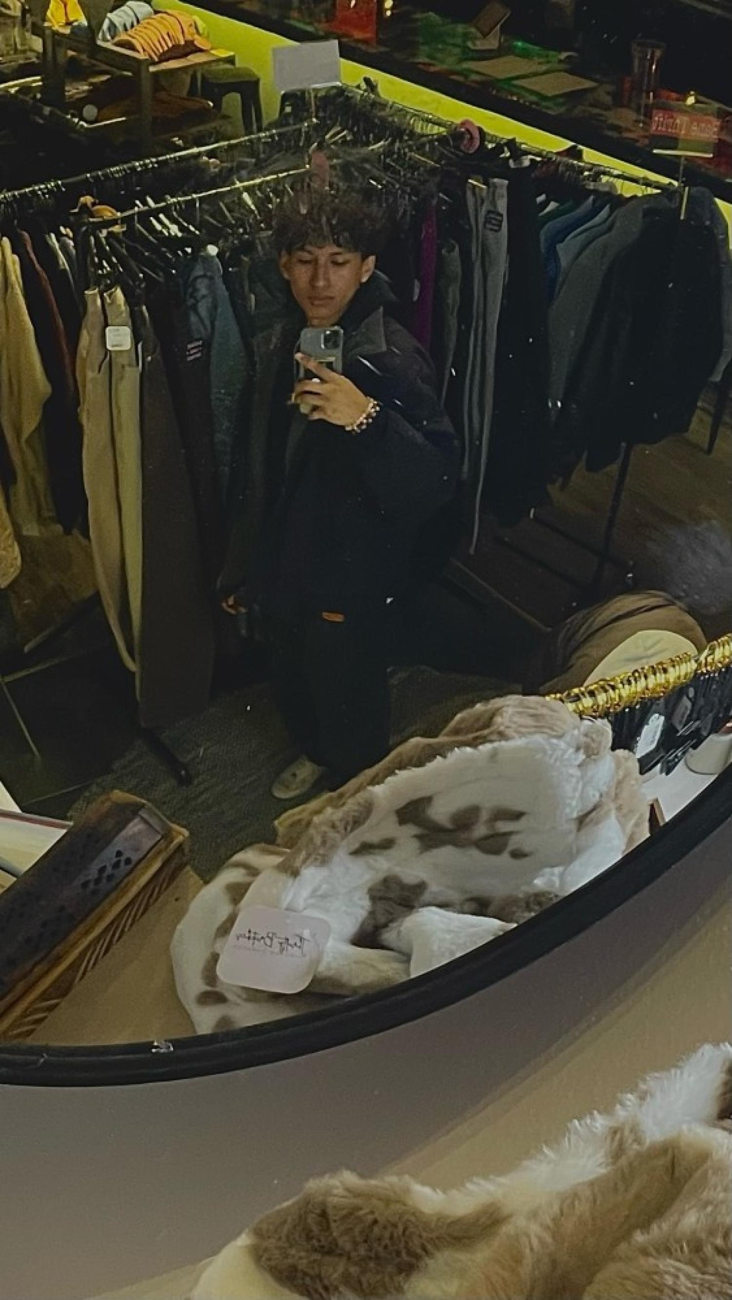 Irving. He is standing amidst clothing racks in a store. He has light brown skin and dark hair.