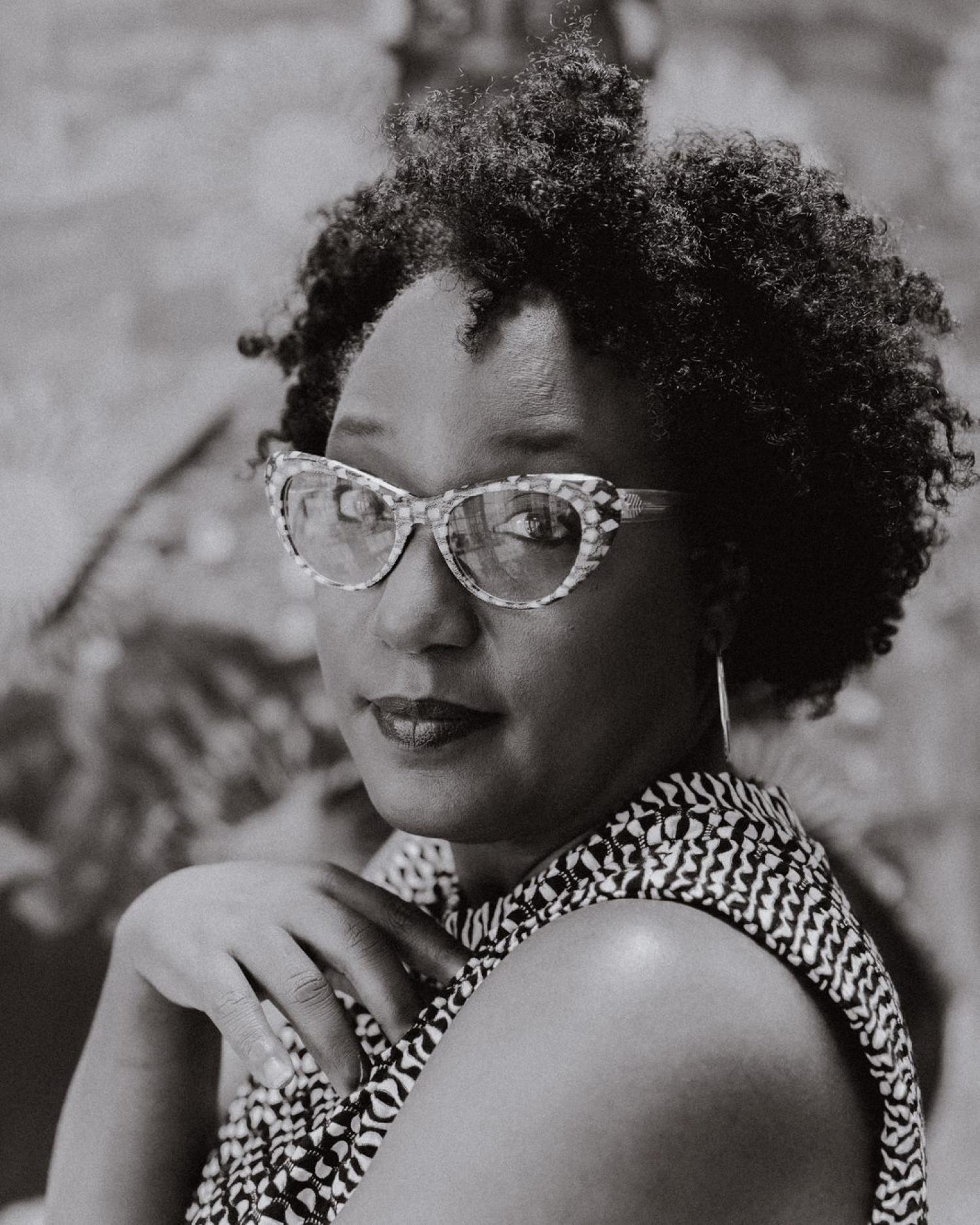 Delita Martin. She is a black woman and has dark, curly hair and patterned cateye glasses.