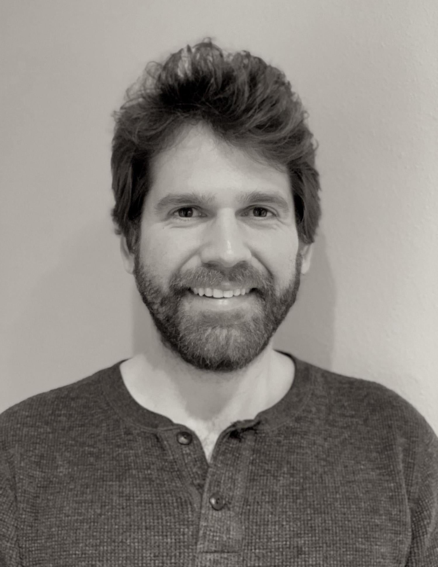 Photograph of Johnny Plastini. He is white and has dark hair and a beard. He is smiling.