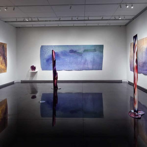 3 large paintings with tall cylindrical sculptures in the foreground. 