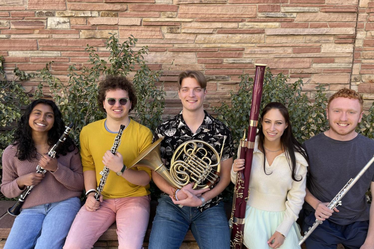 Five students seated outside of a red brick building, all holding different wind instruments.
