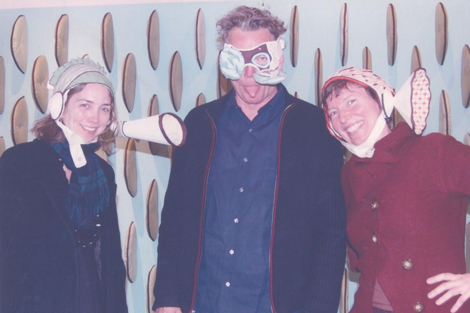 Three people standing next to each other wearing whimsical hats and masks. They are making silly faces. They are, from left to right: Kim Dickey, Scott Chamberlain, and Jeanne Quinn.