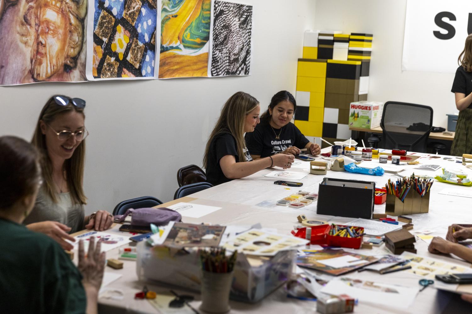 Many students sitting around a table with lots of art supplies while they craft together.