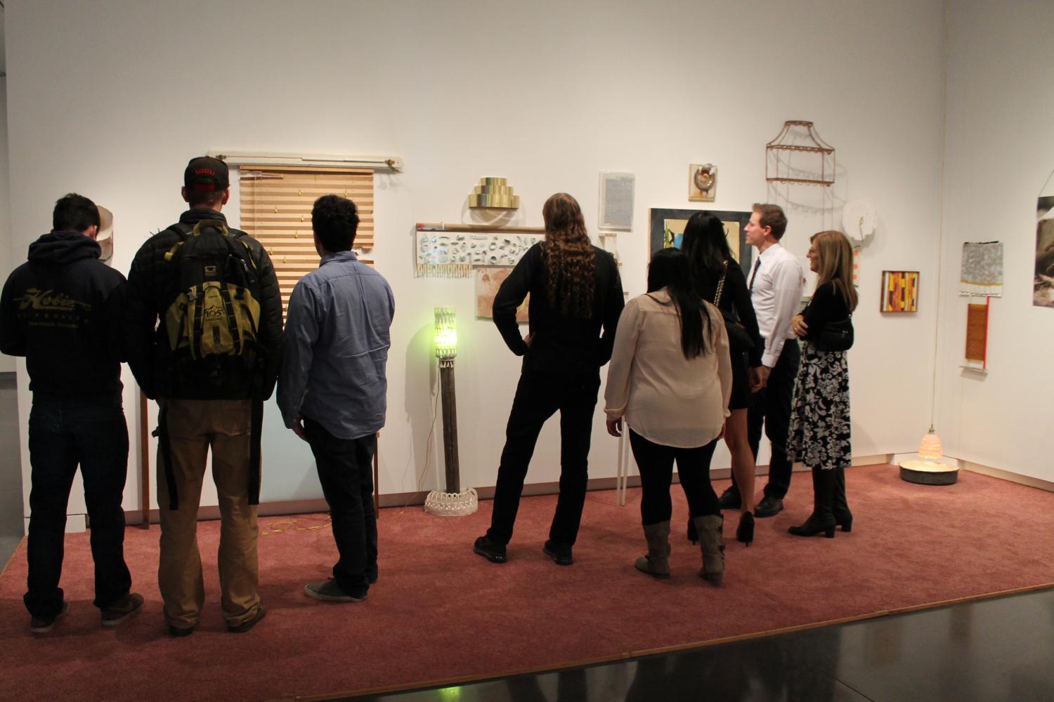 a group of people viewing objects on the wall of the gallery.