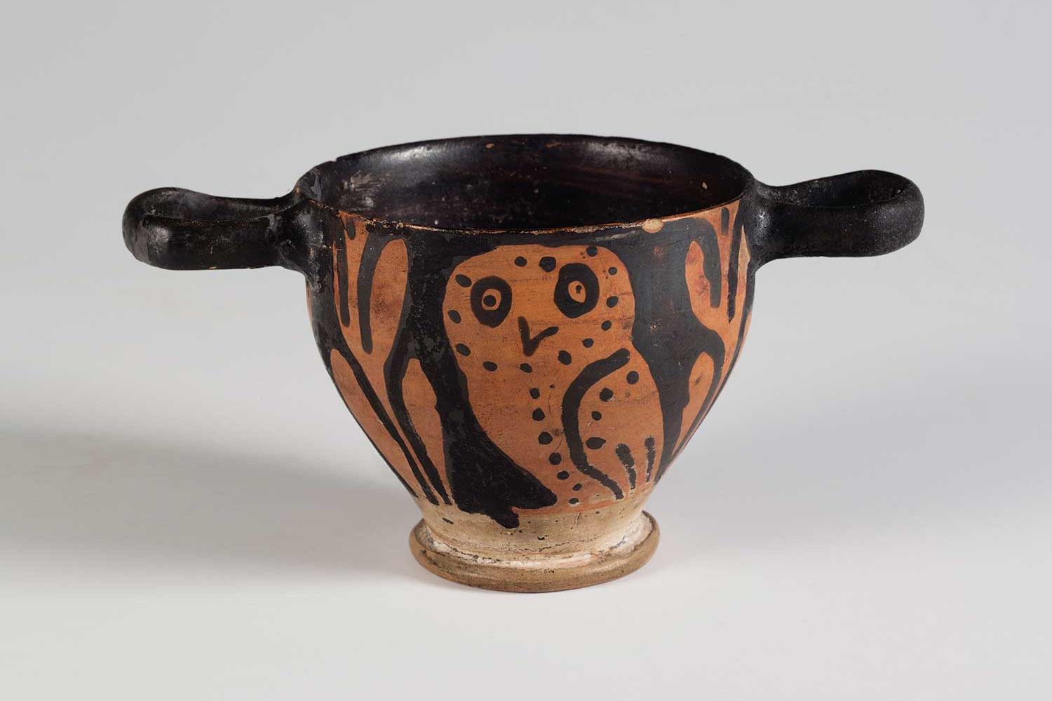Small black cup with a horizontal handle on each side of the rim, decorated with orange owl.