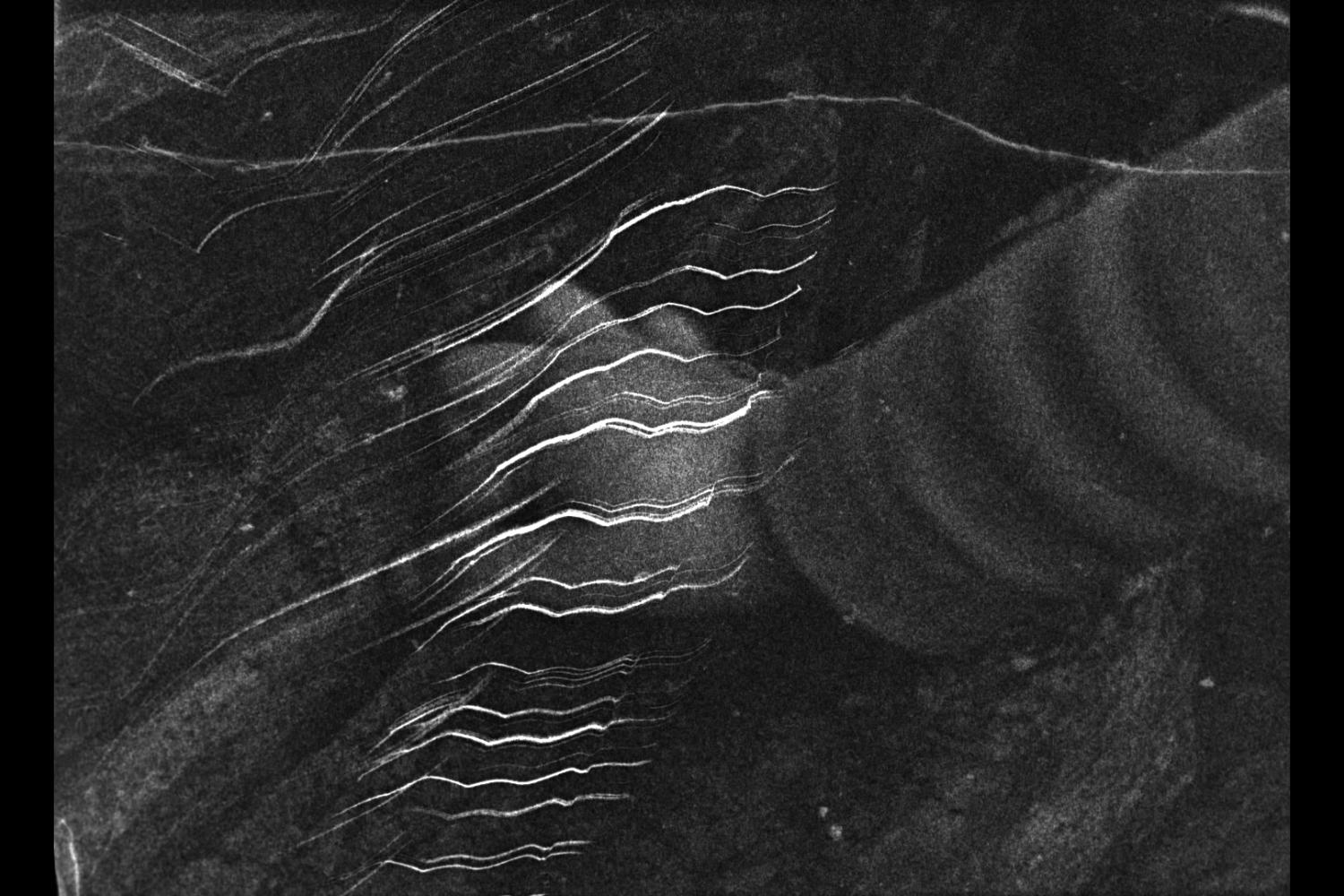 An abstract black and white image featuring white and grey lines over a dark grey and black background with a grainy texture throughout.