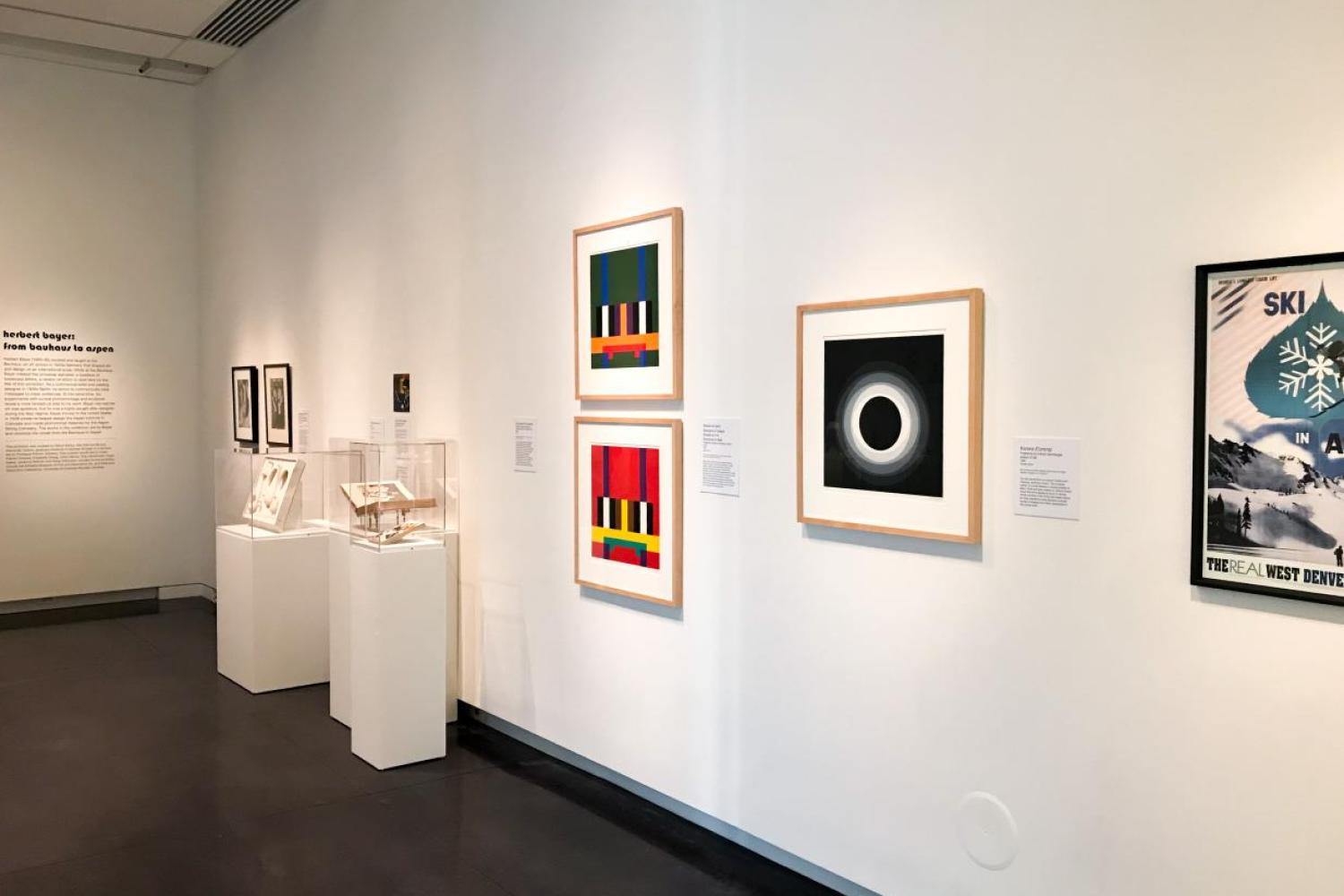 Installation shot of "Herbert Bayer: From Bauhaus to Aspen." A corner of the C-U Art Gallery with many framed artworks hanging from the walls or resting on pedestals.