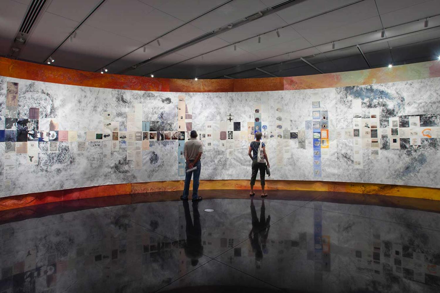 Installation view of two people standing in front of a curved wall
