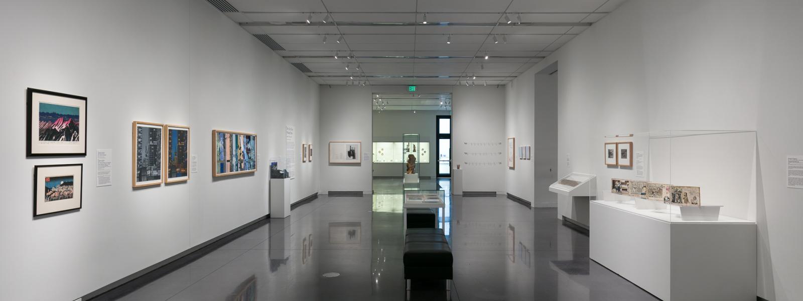 A long CU Art Museum gallery with many artworks hanging on the walls or resting atop white pedestals.