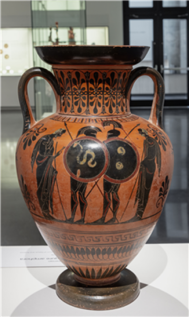 An amphora with black figures on either side. The vessel is mostly reddish and there is a variety of black decoration throughout.
