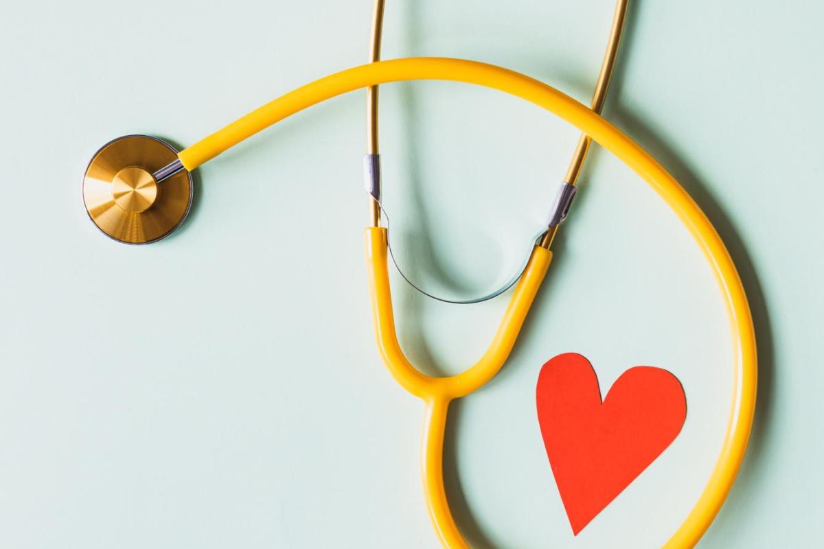 A yellow stethoscope and red paper heart against a blue background.