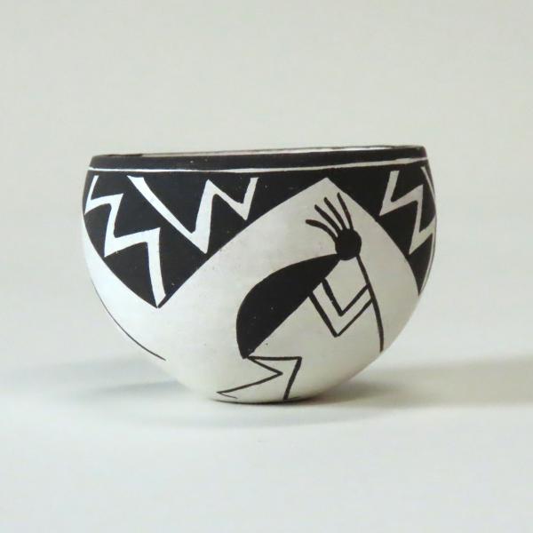 small rounded clay bowl with black and white designs of person playing flute