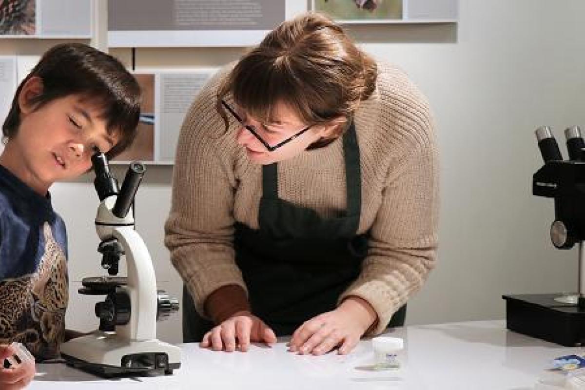 Student showing microscope to young child