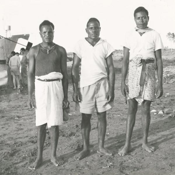 Three native men standing on beach, wearing some western clothes