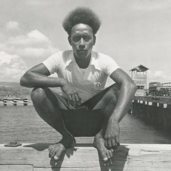 Man squatting on wooden dock railing.