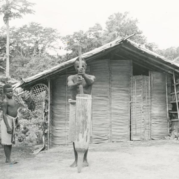 Man mashing wood pole into wooden cylindrical vessel