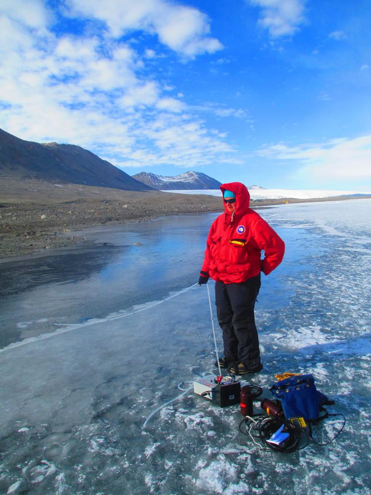 Researcher standing on lake ice with scientific instruments nearby